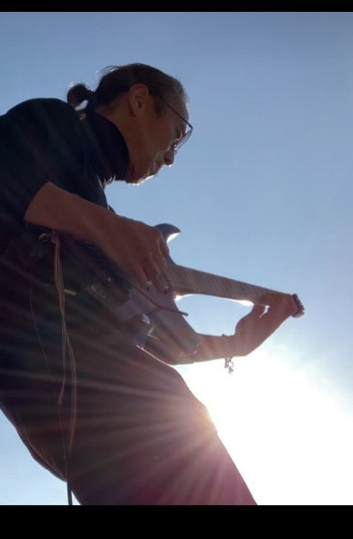 Peter Fujii playing electric guitar in the sunlight.